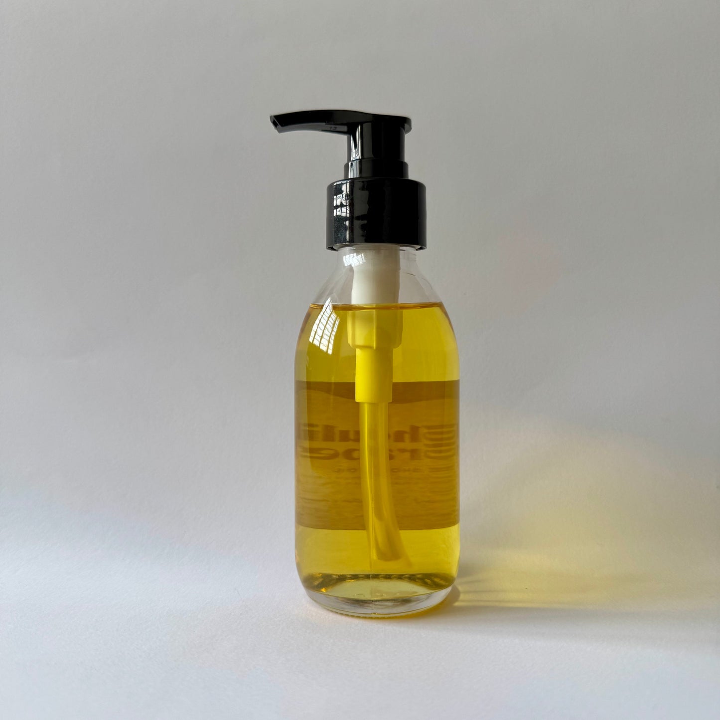 Bottle of yellow liquid shower oil with a black pump on a white background