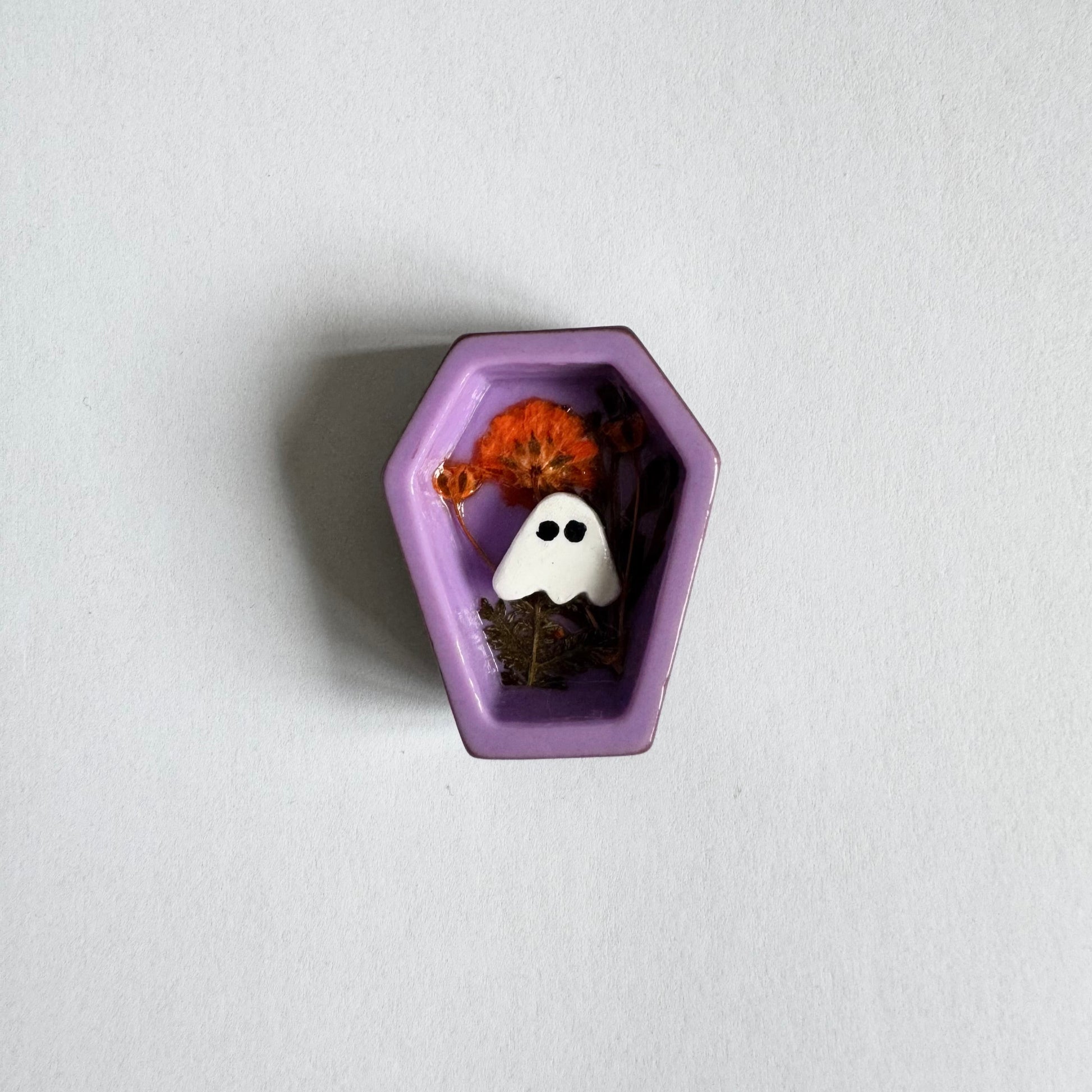 Small decorative item shaped like a purple coffin with a ghost and pumpkin on a white background