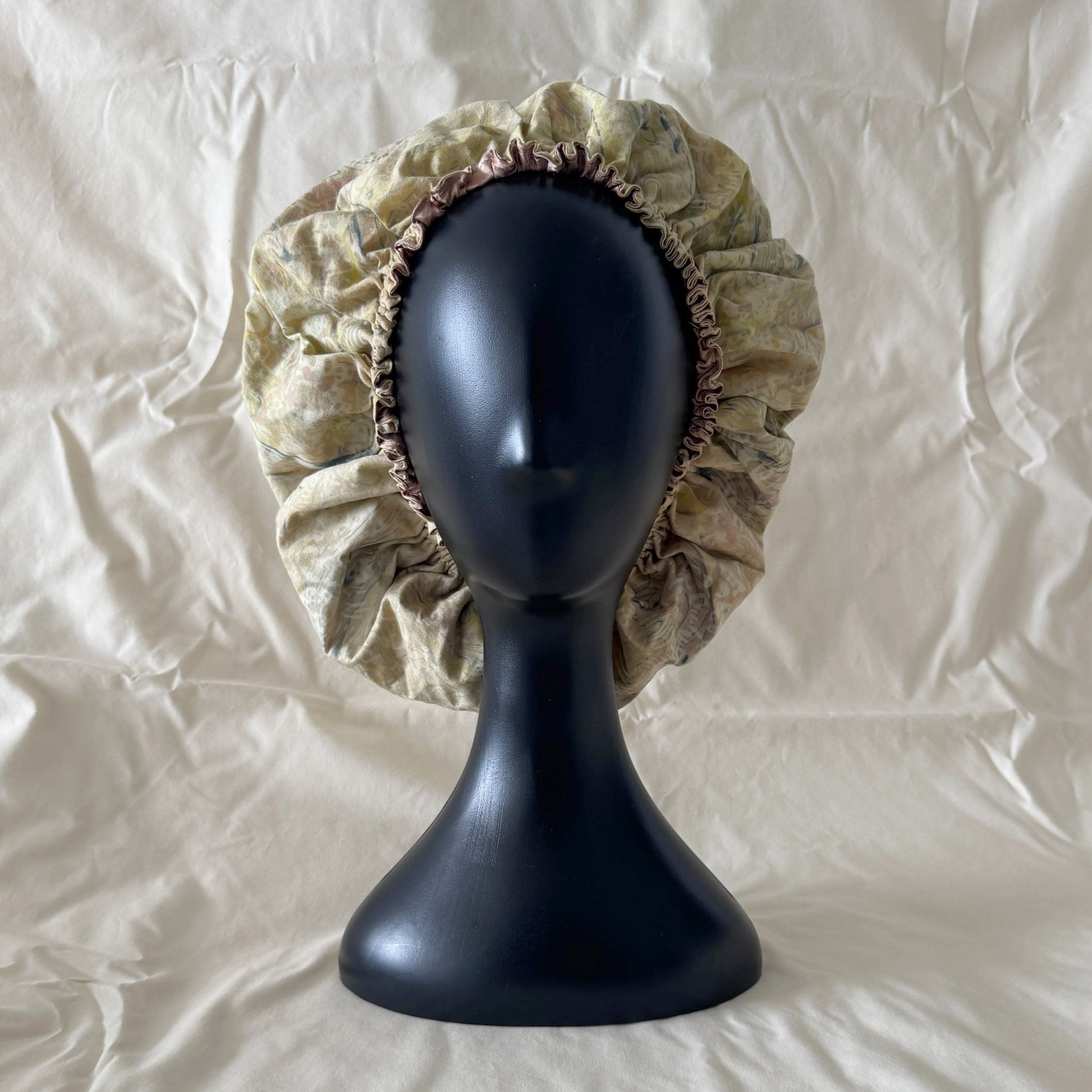 Beige batik sleep bonnet on a black mannequin head against a white background