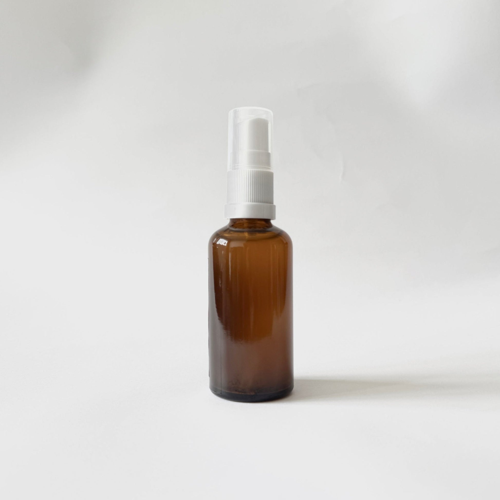 Brown glass spray bottle with white nozzle on a light gray background
