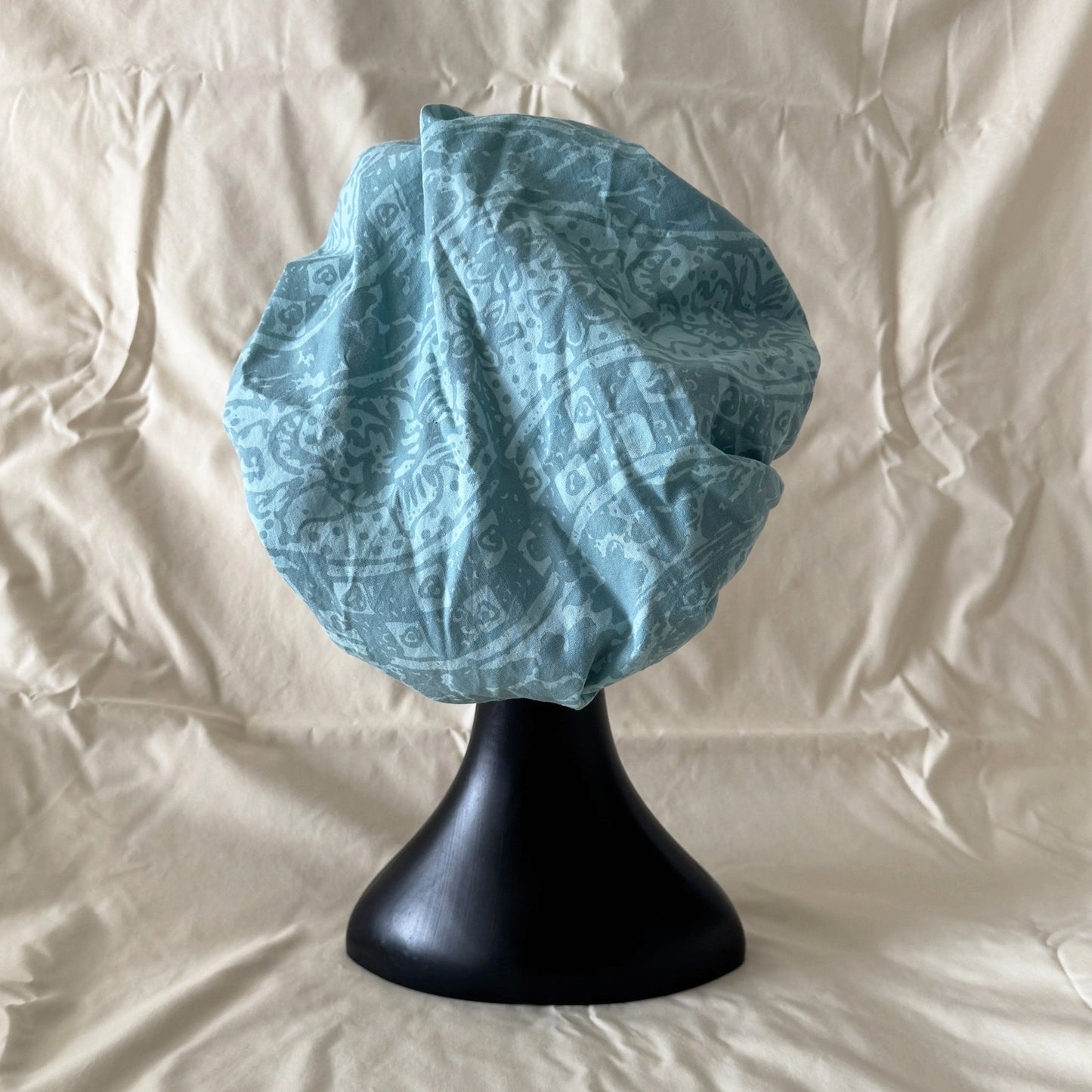 Blue batik elastic sleep bonnet on a black stand against a beige background